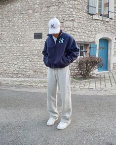 a man standing on the street in front of a building wearing a yankees sweatshirt and sweatpants