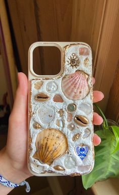 a person holding up a cell phone case with shells and seashells on it