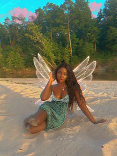 a woman sitting in the sand with wings on her head