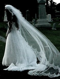 a woman in a wedding dress and veil is walking through the grass near a grave