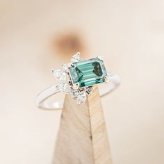 an emerald and diamond ring sitting on top of a wooden stand