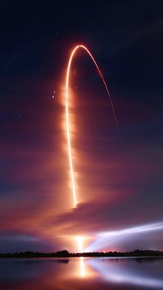 a long exposure shot of a rocket taking off into the night sky with its reflection in the water