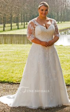 a woman standing in front of a lake wearing a wedding dress with sleeves on it