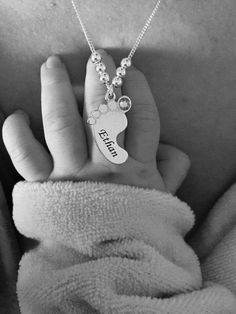 a baby's hand holding a silver necklace with a dog paw and name on it