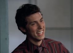 a young man wearing a striped shirt and tie smiles at the camera while looking to his left