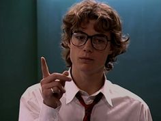 a young man wearing glasses and a tie making the v sign with his fingers while standing in front of a green wall