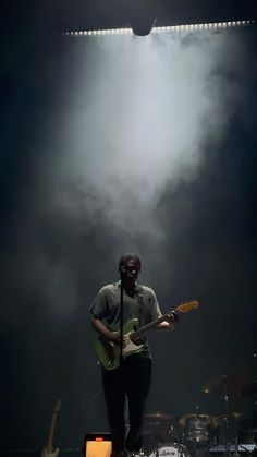 a man with a guitar standing in front of a microphone and some lights behind him