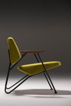 a yellow chair sitting next to a wooden table on top of a gray floor in front of a black wall