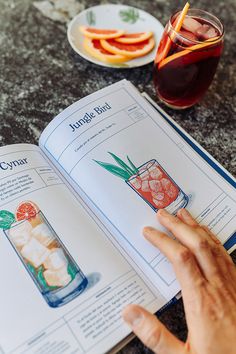 a person is reading a recipe book on a table with drinks and plates in the background