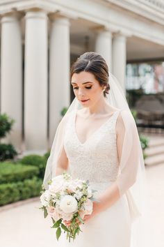 a woman in a wedding dress holding a bouquet and looking down at her hand while wearing a veil