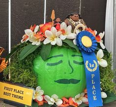 a green face with flowers on it and a blue ribbon around its neck is surrounded by other decorations