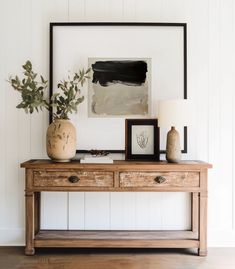 a wooden table with two vases on top of it next to a framed painting