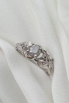 a diamond ring sitting on top of a white cloth with leaves and vines around it