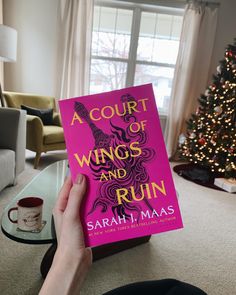 a person holding up a book in front of a christmas tree