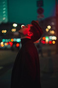 a man standing on the street with his head turned to the side and lights in the background