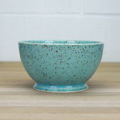 a small blue bowl sitting on top of a wooden table next to a white brick wall