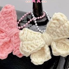 there are two knitted bows on top of a black purse, one pink and the other white