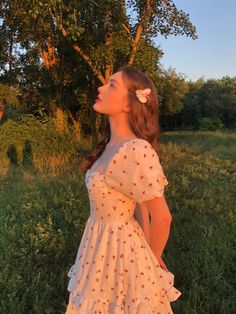 a woman standing in the grass wearing a white dress with red flowers on it's back