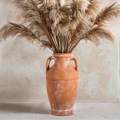 an orange vase filled with dry grass on top of a table