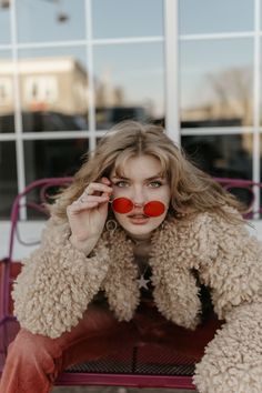 a woman sitting on top of a bench wearing a coat and red clown nose rings