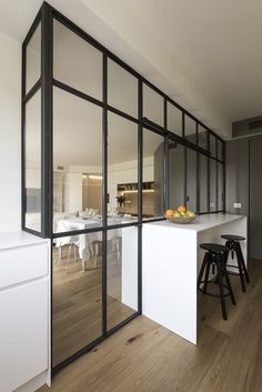 an open kitchen and dining room area with white walls, wood flooring and black framed glass doors