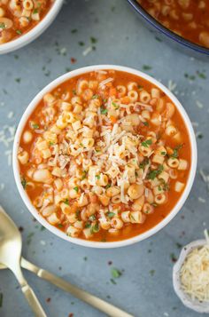 two bowls of pasta soup with cheese and parmesan on the side next to spoons