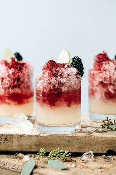 three glasses filled with ice and berries on top of a wooden table