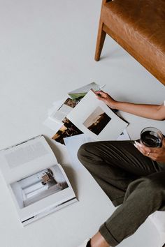 a person sitting on the floor with some books and wine glass in their hand as they look at photos