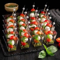 many small trays filled with food on top of a wooden table next to tomatoes and basil