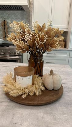 a candle and some dried flowers on a table in a kitchen with white cupboards