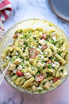 a glass bowl filled with pasta salad on top of a marble counter next to a red and white striped towel