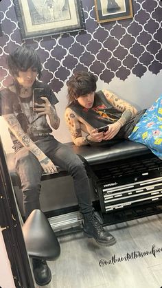 two people are sitting on a bench in front of a mirror and looking at their cell phones