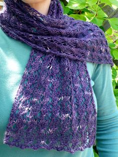 a woman wearing a purple knitted shawl in front of some trees and bushes