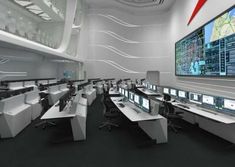 an office with multiple desks and large screens on the wall above them are computers