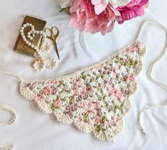 a crocheted purse next to a bouquet of flowers on a white tablecloth