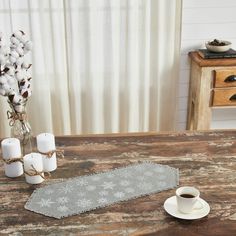 a wooden table topped with a cup of coffee next to a vase filled with flowers