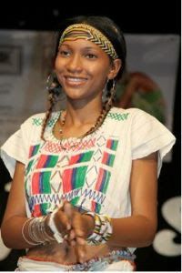 a woman with braids is smiling and holding something in her hands while wearing an african headdress