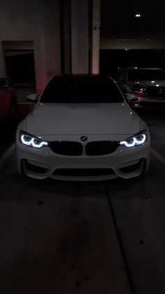 a white car parked in a parking lot at night with its headlights turned on and glowing