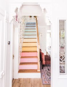 an open door leading to a living room with white walls and wood floors, along with colorful stair treads