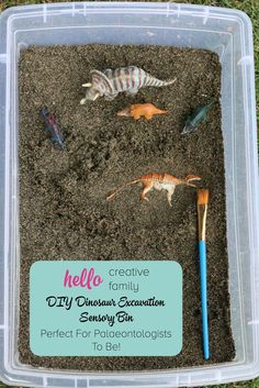 a plastic container filled with dirt and small toy dinosaurs in the sand next to a blue toothbrush