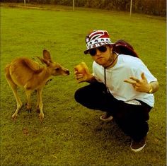 a man is feeding a kangaroo something in his hand while wearing sunglasses and a hat