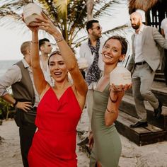 two women in red dresses are holding drinks and posing for the camera with other people behind them