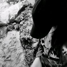 black and white photograph of a woman wearing a hat on top of a rock wall