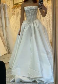 a woman taking a selfie in front of a mirror wearing a white wedding dress