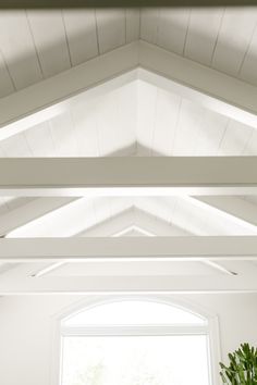 a room with white walls and wooden beams on the ceiling is filled with potted plants