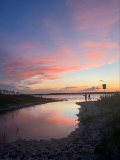 two people are standing on the shore at sunset