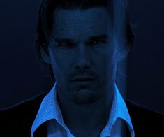 a man wearing a white shirt and black jacket in the dark with blue light coming from behind him