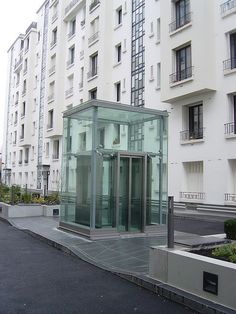 a glass enclosed area in front of a white building with balconies on the sides