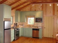 a kitchen with green cabinets and wood flooring in a cabin style home on the edge of a lake