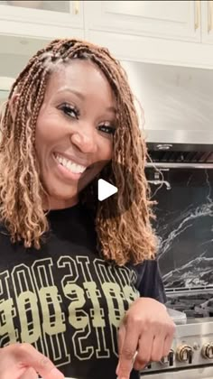 a woman in a black shirt is cooking food on a stove and smiling at the camera